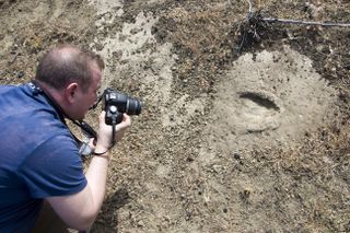 A researcher takes a photo of a footprint for 3D modeling. It's unclear if this print belongs to a human or animal.
