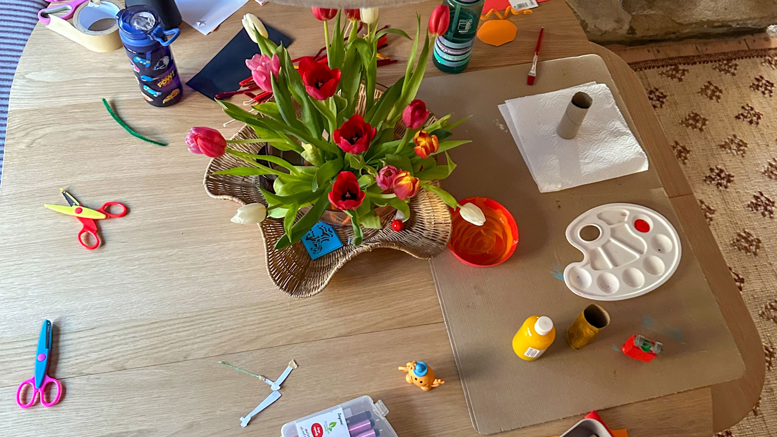 Kitchen table with flower arrangement, kids crafting materials and paint as seen from above