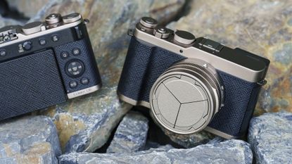 The Gold Titanium Special Edition of the Panasonic Lumix L10 compact camera, sat on gray and rust-colored rocks