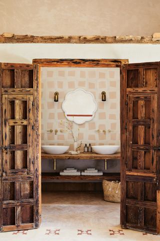 A rustic bathroom with pink and white geometric tiles, wooden shutter doors and a double vanity