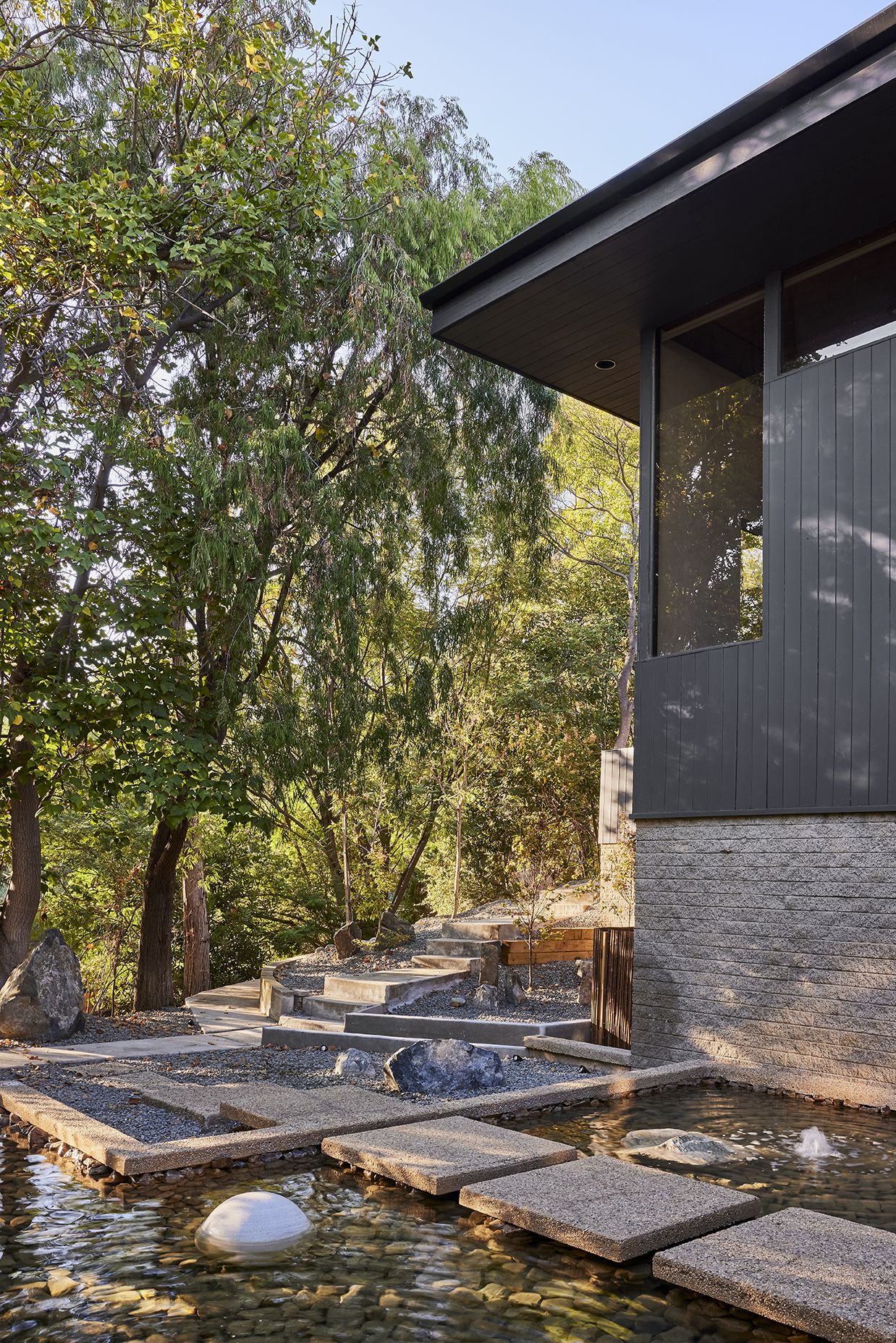 The home's entrance unfolds through a tranquil composition of water, stone, and native planting, creating a meditative threshold between architecture and nature.