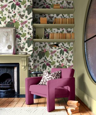 living room with floral wallpaper on chimney breast above cast iron fire, in alcove with green shelves, wooden floor, purple occasional chair and partial view of internal black framed circular window on one wall