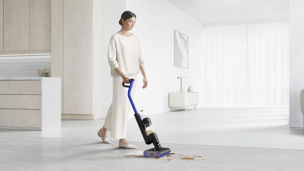 Person wearing white clothes using Dyson WashG1 to clean brown spill on smooth gray floor in minimalist, gray and white home