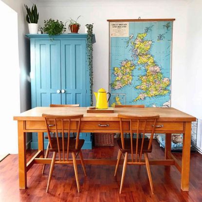 Kitchen with wooden table and chairs in front of blue painted cabinet topped with houseplants beside vintage map of Britain and Ireland hanging on wall