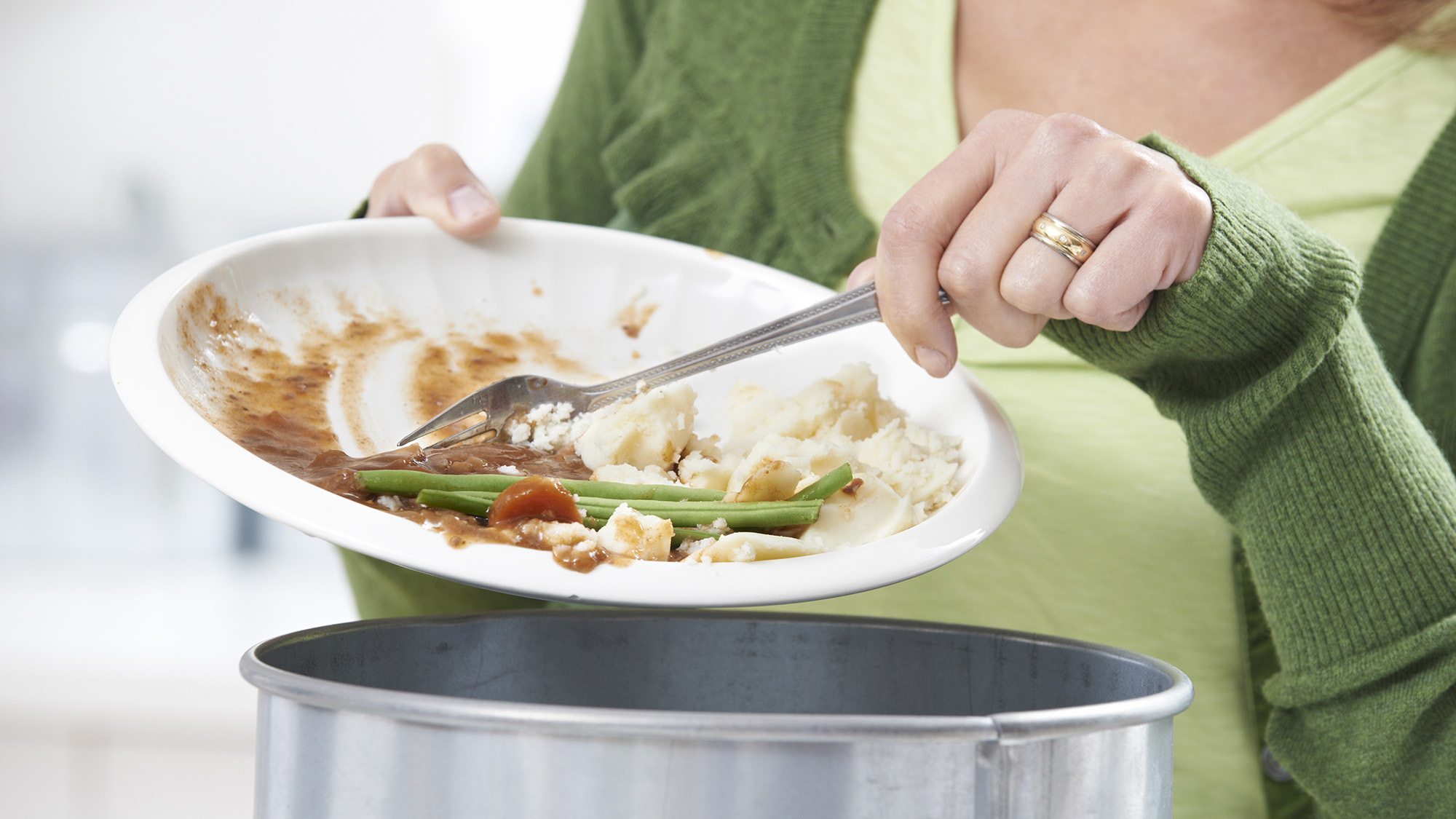 Woman scraping food on plate into a bin