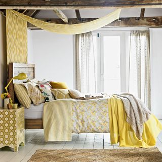 A bedroom with a bed dressed with yellow printed covers and ceiling hanging