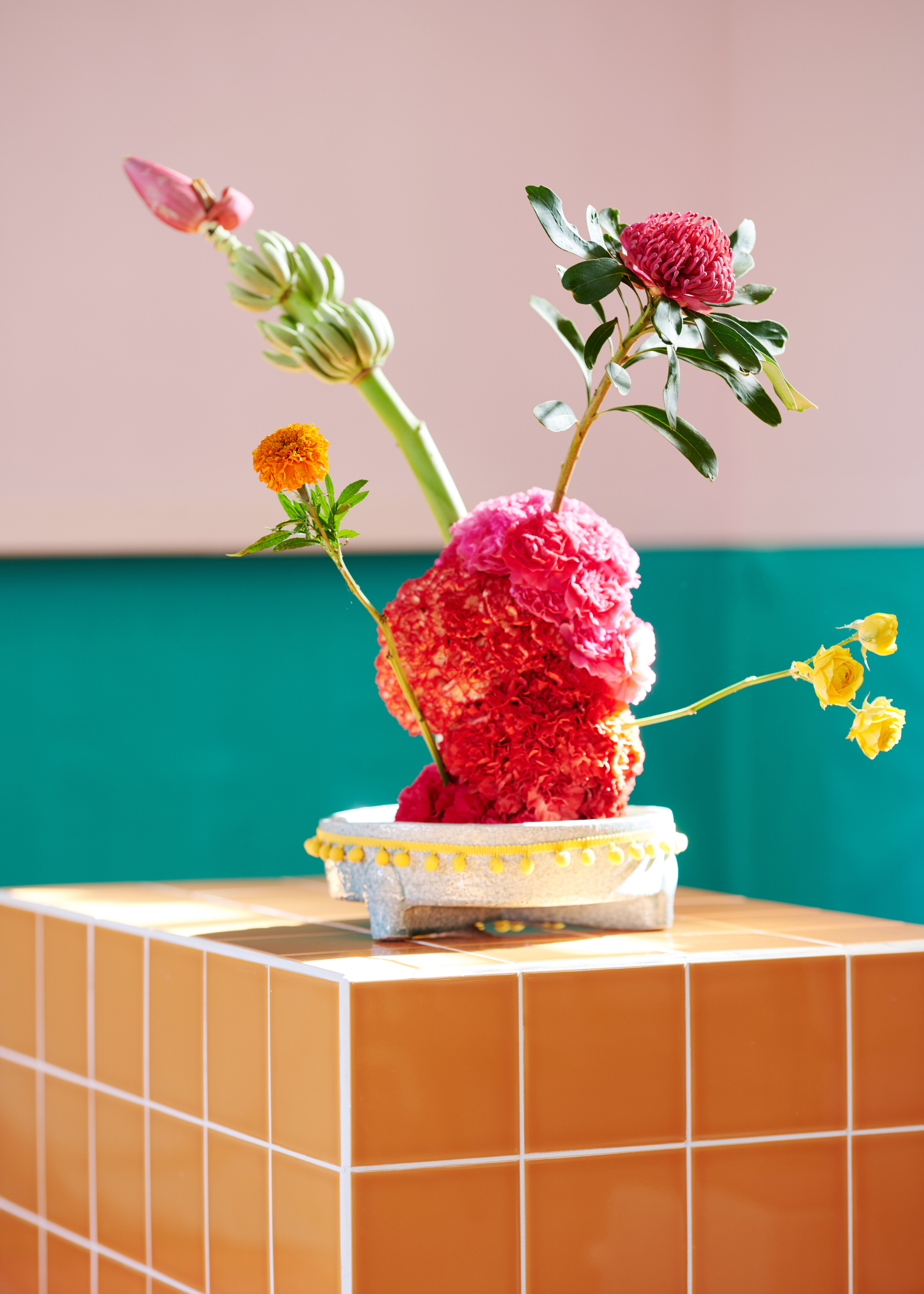 A structural bouquet with marigolds on a tiled side table