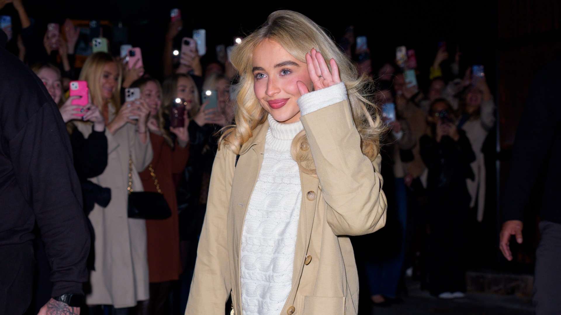 a paparazzi photo of a white woman with blonde hair waving to a crowd of people on the street