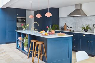 blue kitchen and island with marble countertop, parquet flooring, and three pink pendant lights over the island