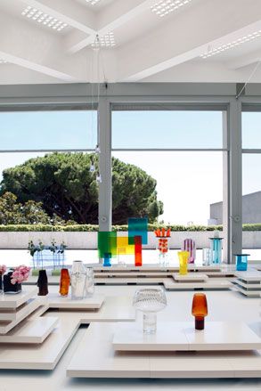 Contemporary glass designs photographed on white platform surfaces with clear glass window panel in the background and views of a big tree outside