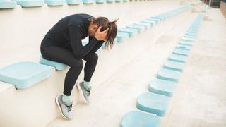 Tired and powerless woman sitting on stadium seat after hard running training
