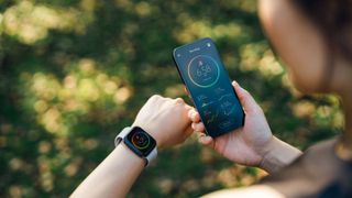 Woman looking down at watch and holding phone with tracking app, representing the best fitness trackers