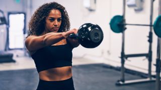 Woman performs kettlebell swing in gym