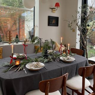 A dining table set for a Christmas dinner with candlesticks decorated with ribbons tied into bows and plates adorned with bow-folded napkins