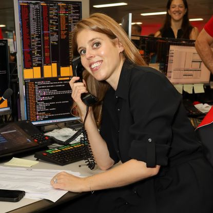 Princess Beatrice wearing a black dress smiling on a phone