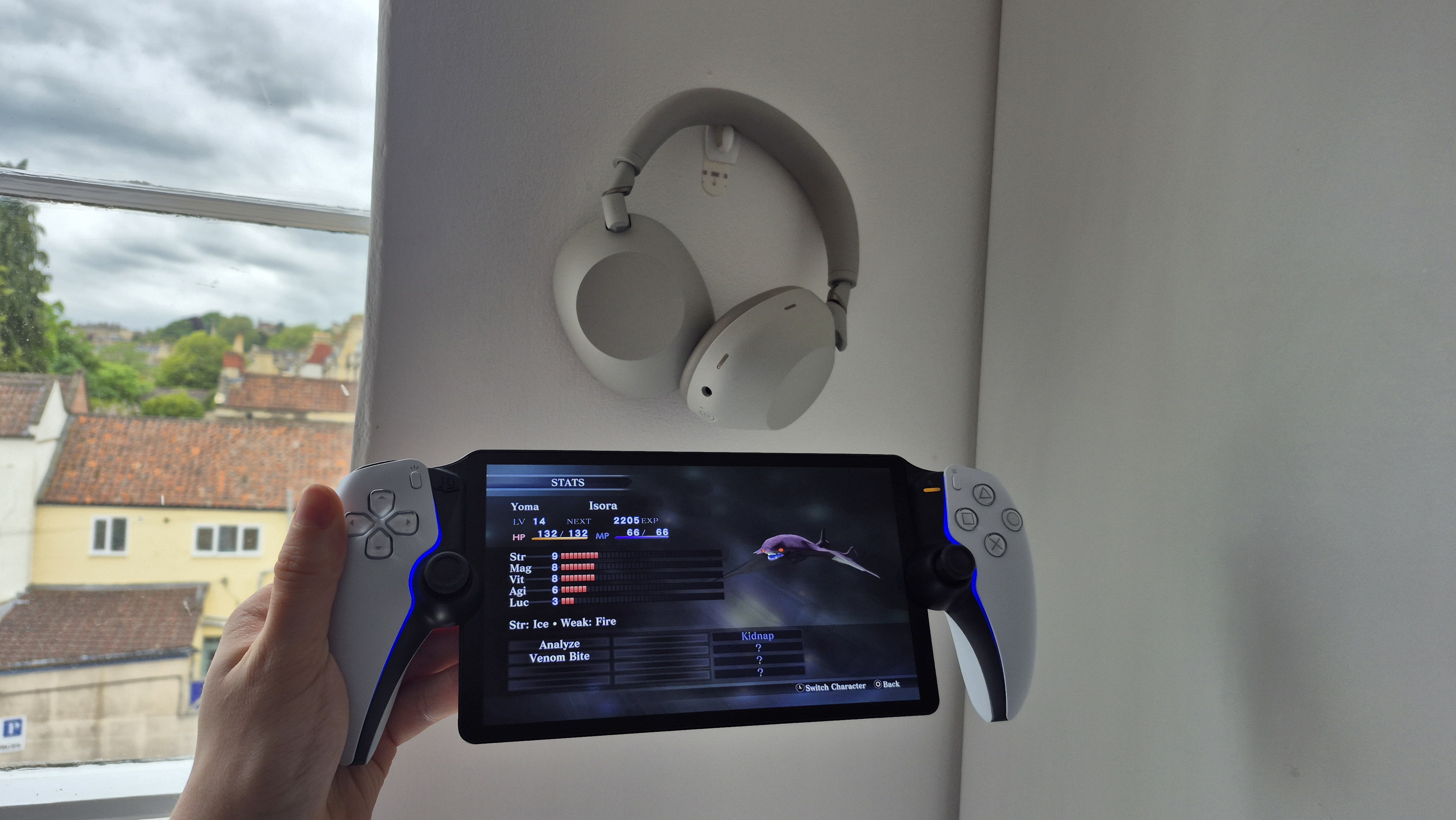 Sony WH-1000XM6 ヘッドフォンの隣で PS Portal を持ち、真・女神転生 III: Nocturne をプレイしている男性