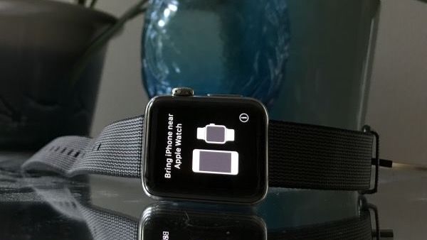 An Apple Watch with a grey strap on a glass table displaying a screen that reads &#039;bring iphone near apple watch&#039;