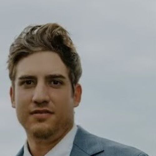 Michael is a white man with dark blonde hair, pictured wearing a light blue suit jacket over a white collared shirt