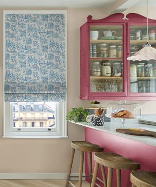 A white kitchen with a pink cabinet, a breakfast bar, and blue blinds