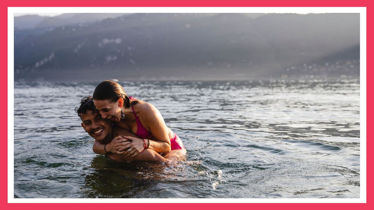 playful couple on top of one another while in a lake with mountains in the background