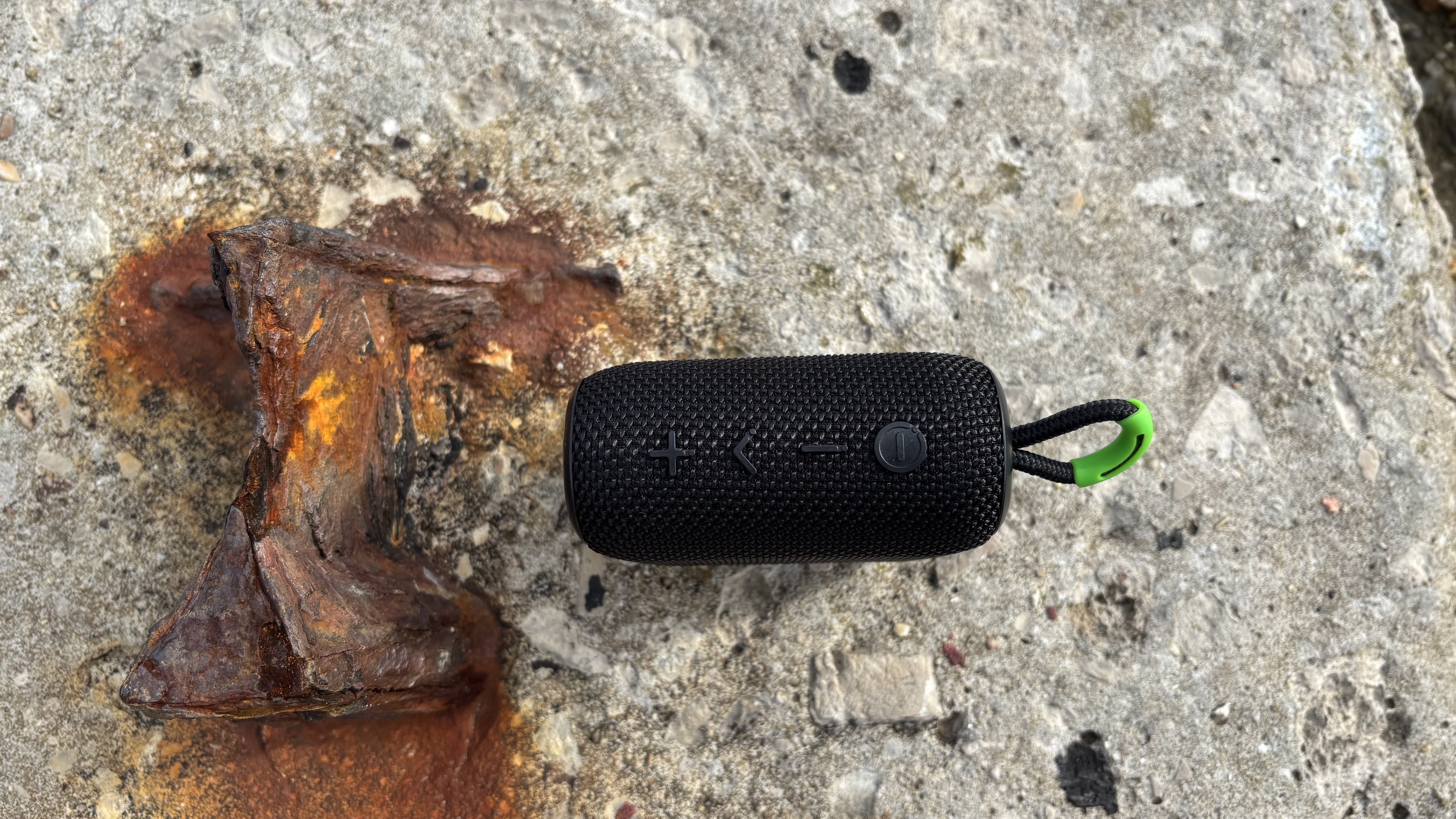 Top panel of the black AO mini portable wireless speaker, showing its four button and hanging loop.