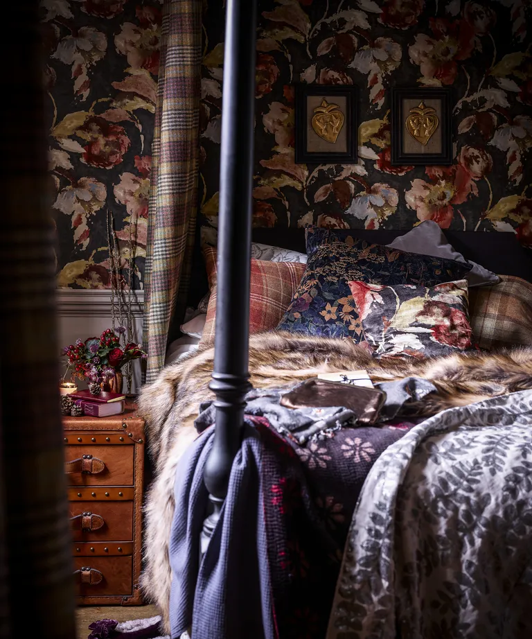 A bedroom with black four poster bed, black and ochre floral wallpaper, and lots of patterned textures