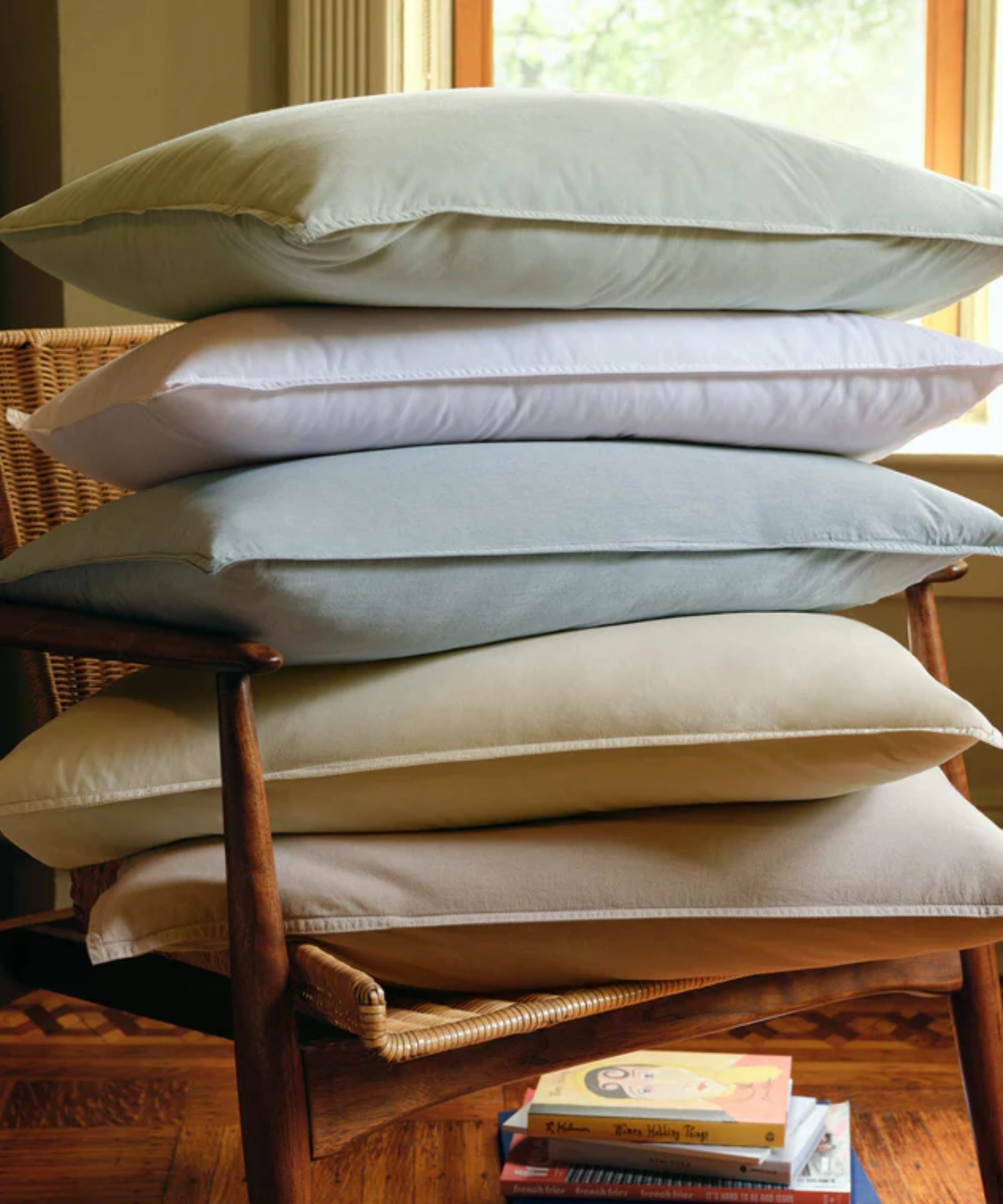 Stack of pale green, blue, yellow and cream pillows on a wicker chair