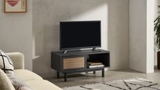 A black wood and vintage cane media unit TV stand with television in living room with Berber rug and cream sofa