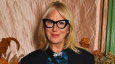 Image of Val Garland smiling with straight, side part blonde shoulder-length hair and wearing black cat-eye frame glasses
