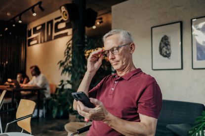 Self-employed man with glasses uses phone in coworking cafe