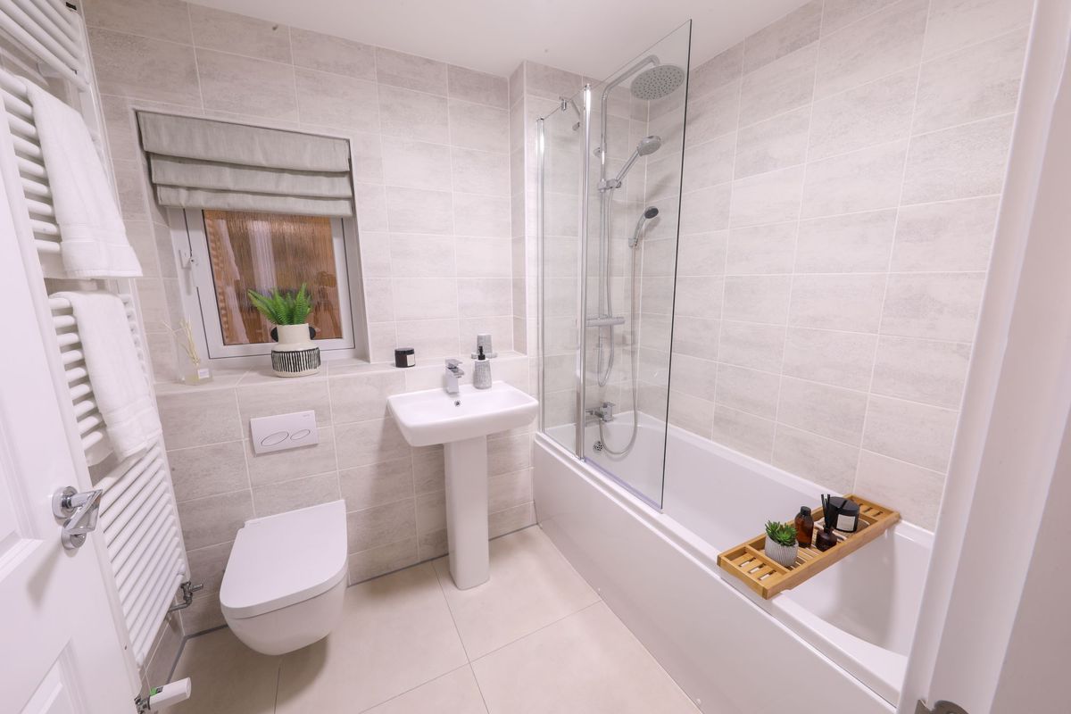 A bathroom with white wall tiles and a shower over the bath