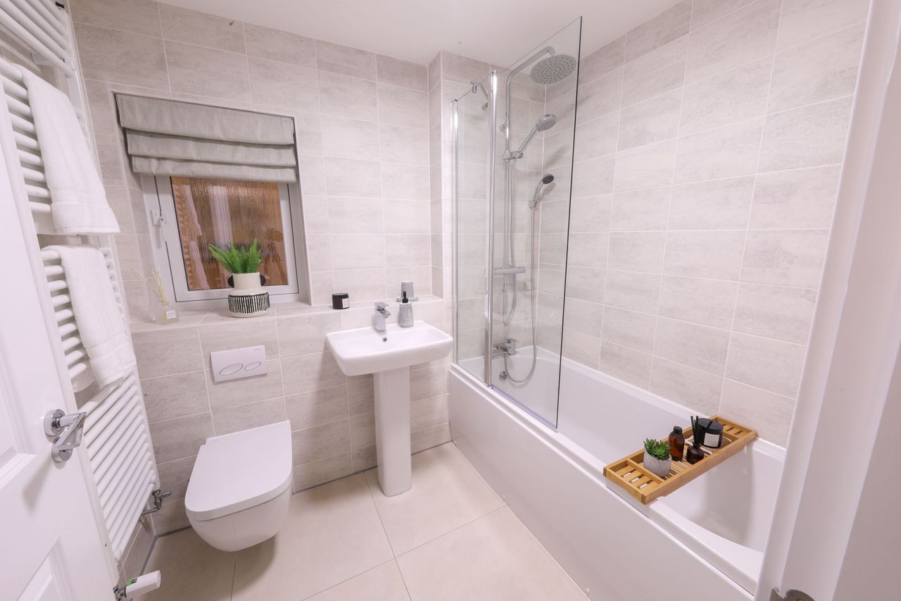 A bathroom with white wall tiles and a shower over the bath