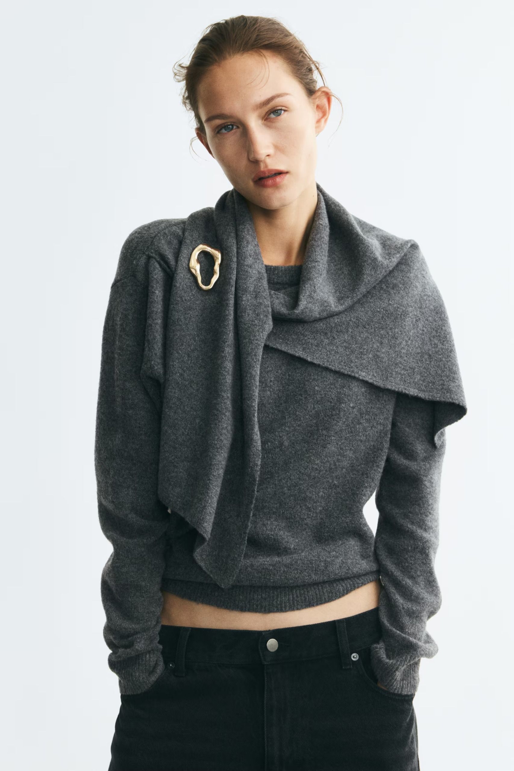 An H&M model wearing a draped grey sweater with a brooch