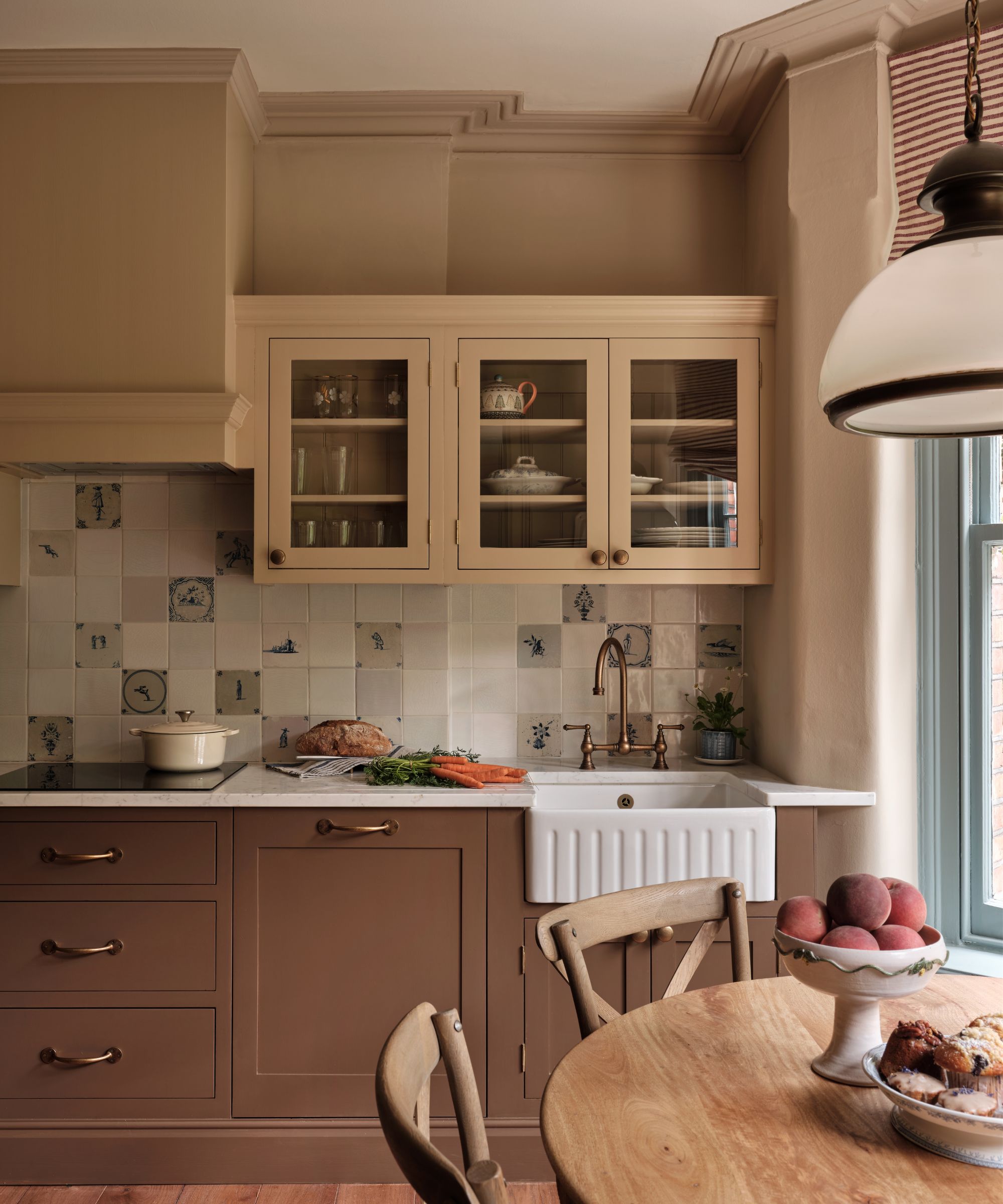Warm beige kitchen featuring a white apron-front sink, patterned blue-and-white tile backsplash, glass-front cabinets, and a round wooden dining table