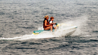 Diana, Princess of Wales, wearing a life jacket over her swimsuit and sunglasses, rides on a jet ski with Prince Harry on July 17, 1997 in Saint-Tropez, France