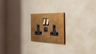 brushed matt brass twin socket on wall with peach mottled effect wallpaper behind