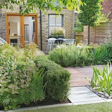 back garden with decked area, paving and planting and grey outdoor chairs