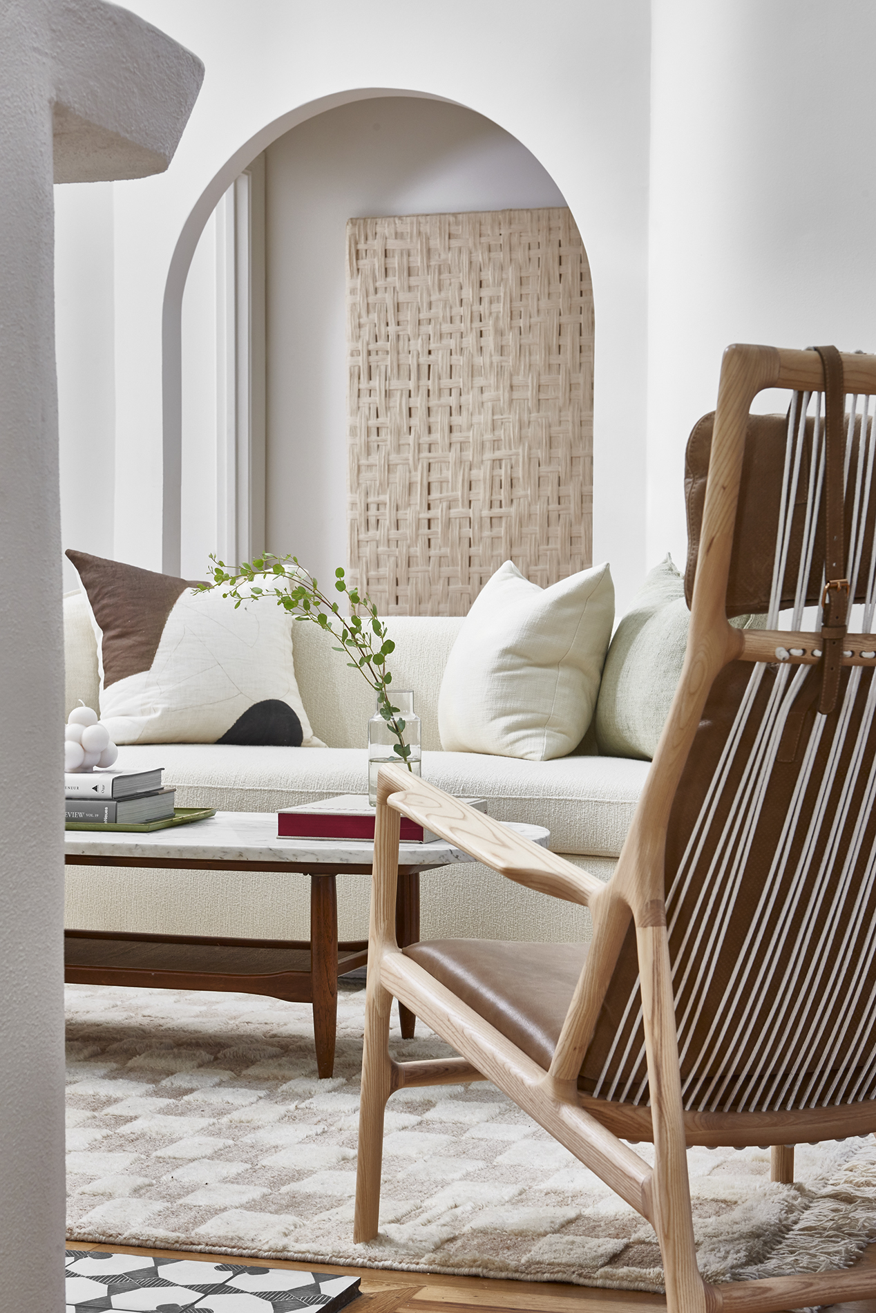 A white, minimalist living room with a white sofa with lots of textures and a wooden and leather accent chair in the corner.