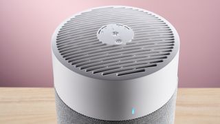 A close-up of the top of Blueair air purifier on a wood surface against a pink background.