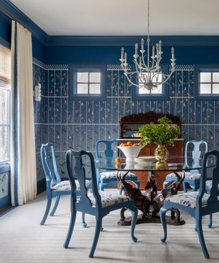 Blue and white dining room with birdcage wallpaper, ornate dining chairs and a white chandelier