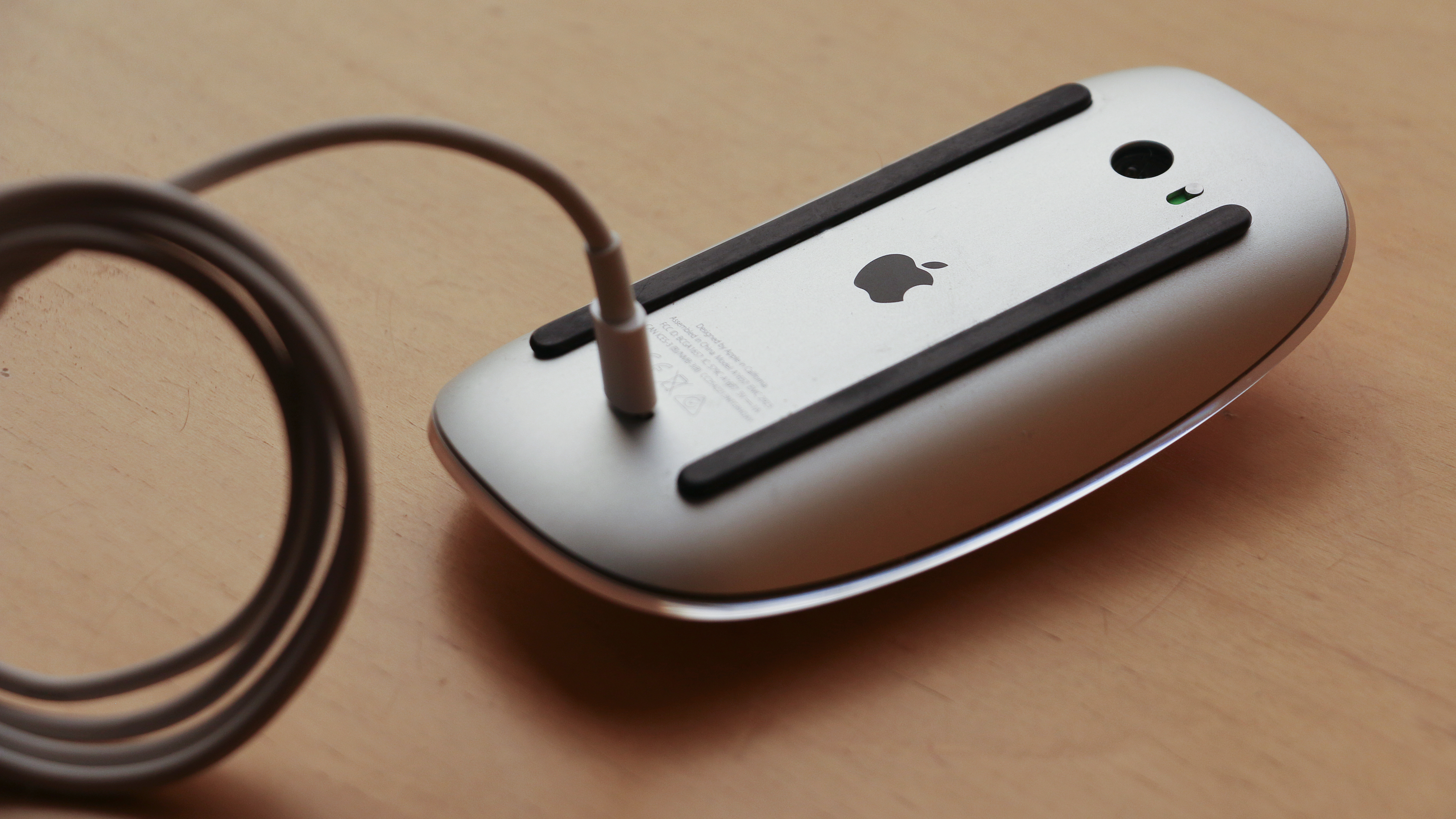 An Apple Magic Mouse on a table upside down being charged