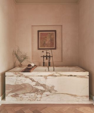 bathroom with light pink walls and marble covered bath