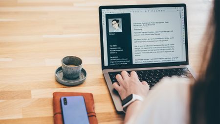 Job application concept image showing woman in a coffee shop updating her CV on a laptop computer.