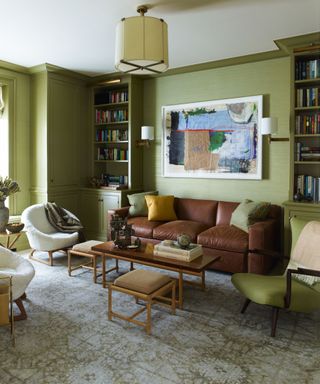 a soft retro avocado green living room with bookshelves and a large brown leather couch