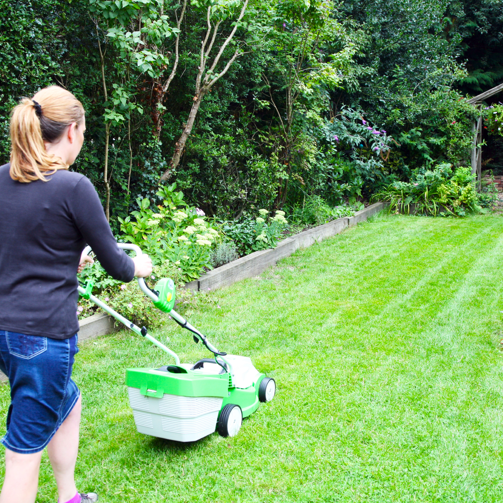 young woman mowing grass in the garden with a lawn mower as part of a good lawn care routine