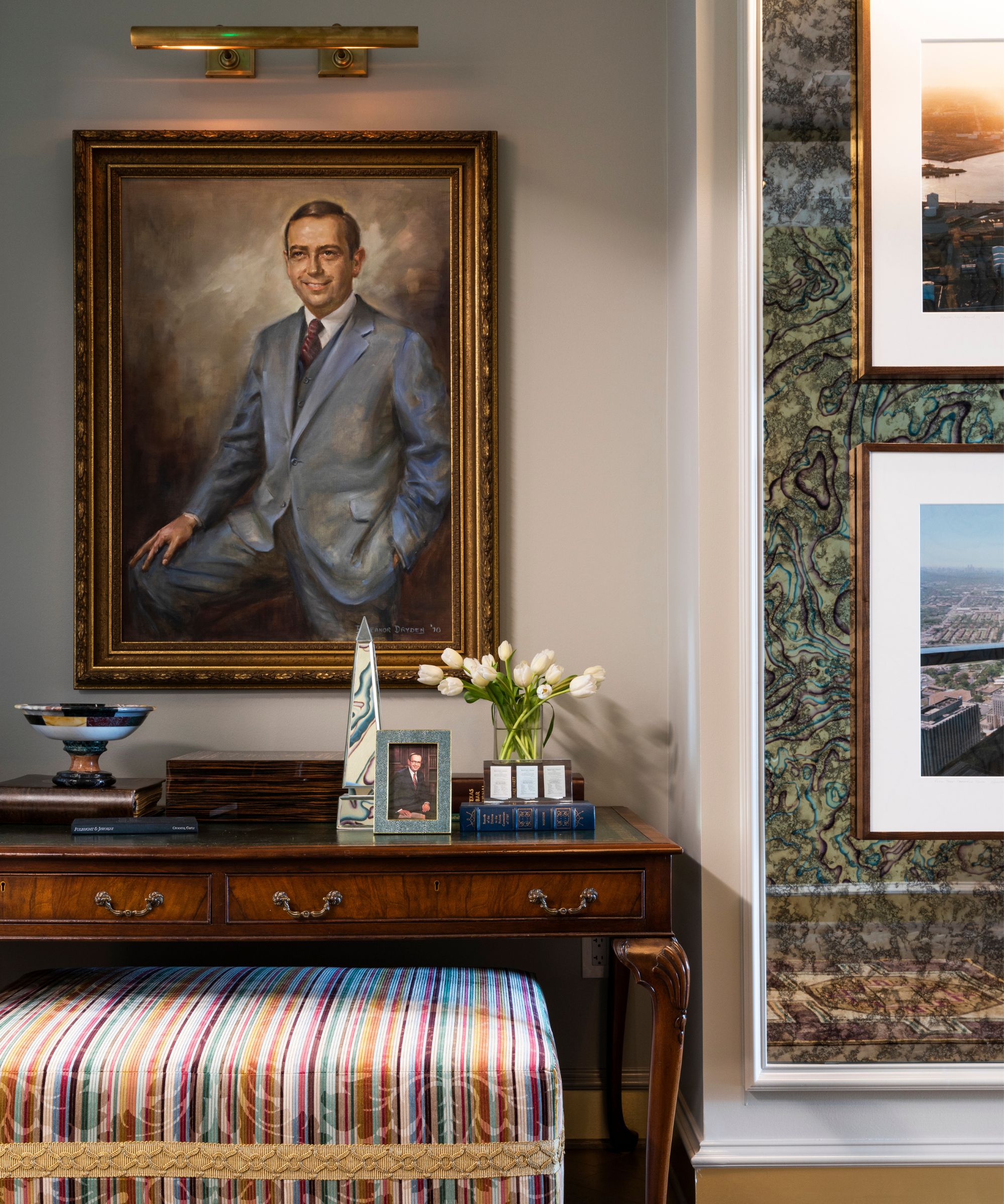 entryway styled with a vintage family portrait with a striped ottoman, antique entry table and a brass picture light