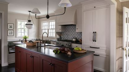 white farmhouse style kitchen with a blue patterned tile backsplash, red kitchen island with dark countertops, breakfast nook in the corner beneath the windows and white and black vintage style lighting