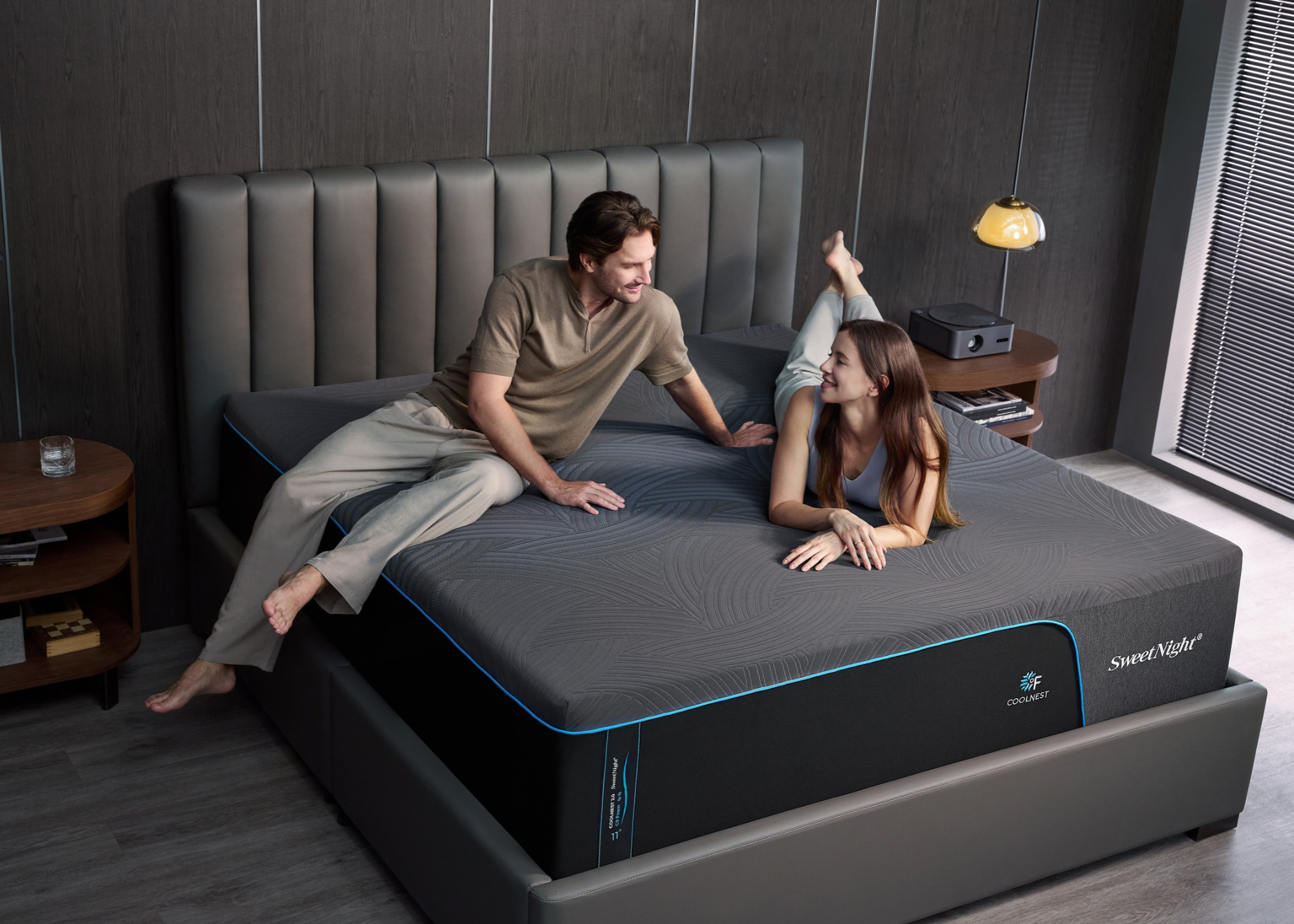A bedroom with a man and a woman sitting on a cooling mattress