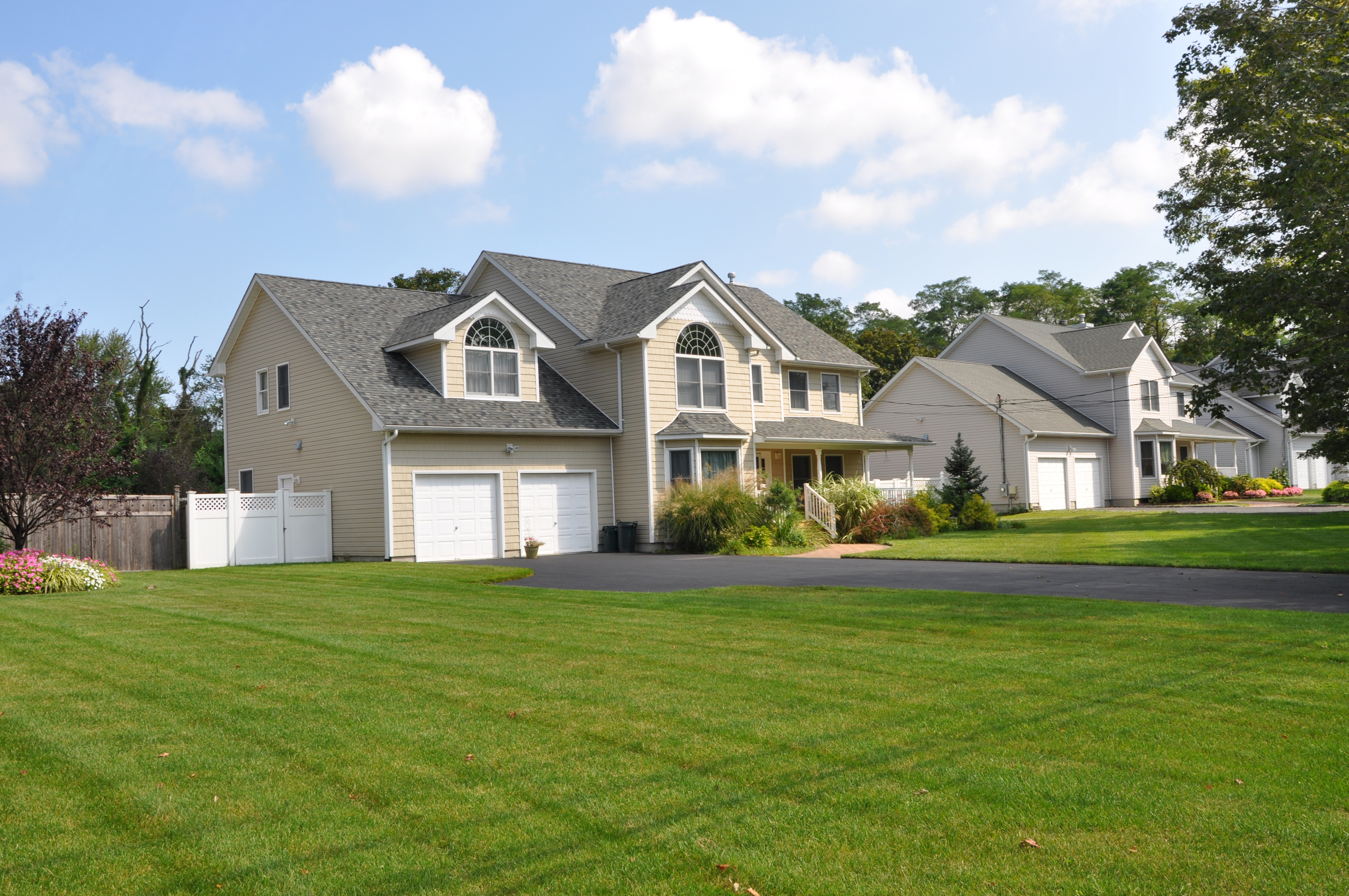 Suburban cream-colored home with an extensive front lawn, blue skies, and shrubbery