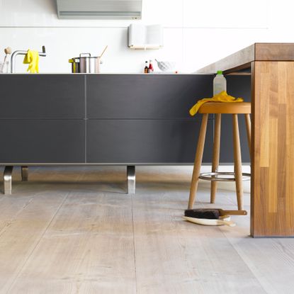 Wooden flooring with a dustpan and brush on it, and a stool with cleaning products on it